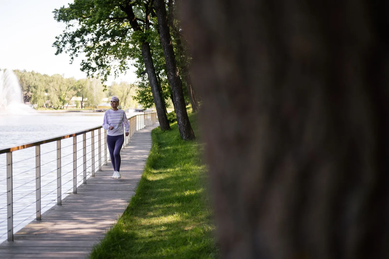 A senior woman enjoys a healthy walk on a lakeside boardwalk on a sunny day.