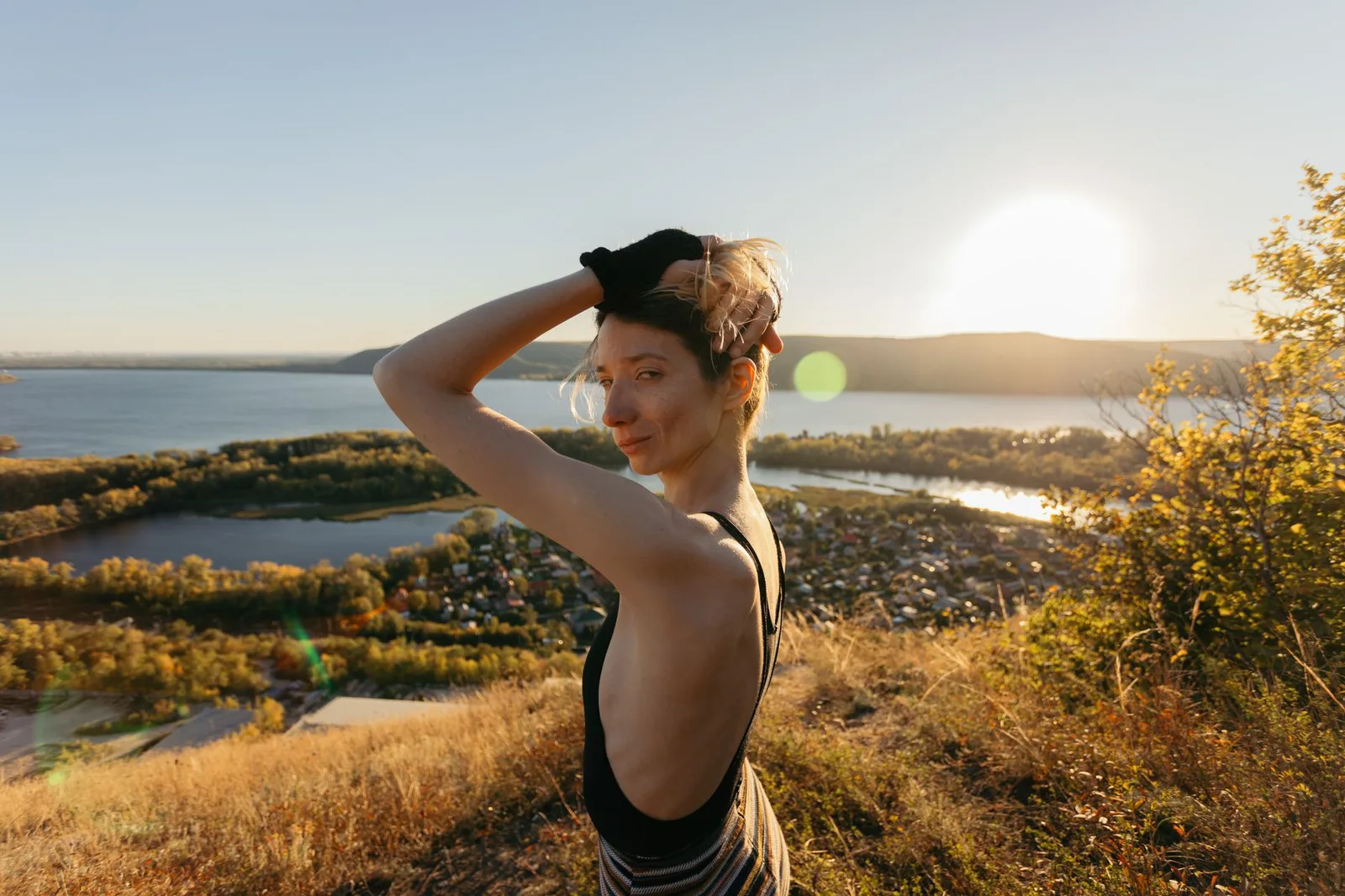 A woman poses on a hilltop overlooking a lake at sunset, exuding freedom and serenity.