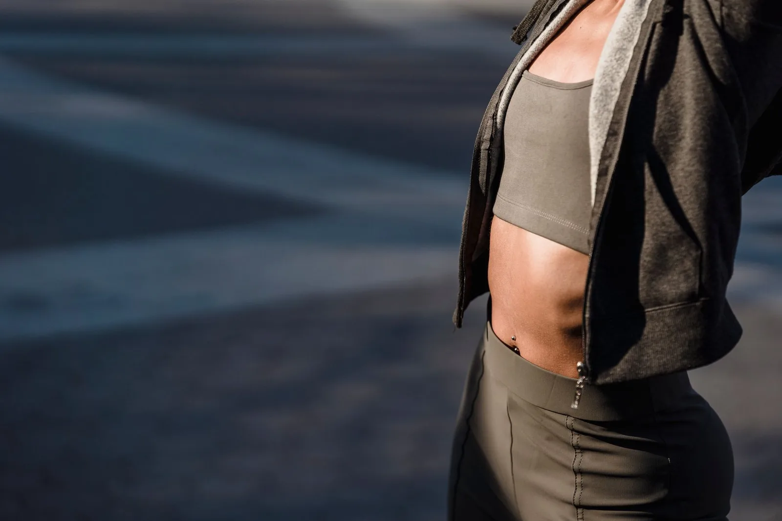 Crop anonymous slim female wearing trendy activewear with top standing on paved sidewalk during training on street of city