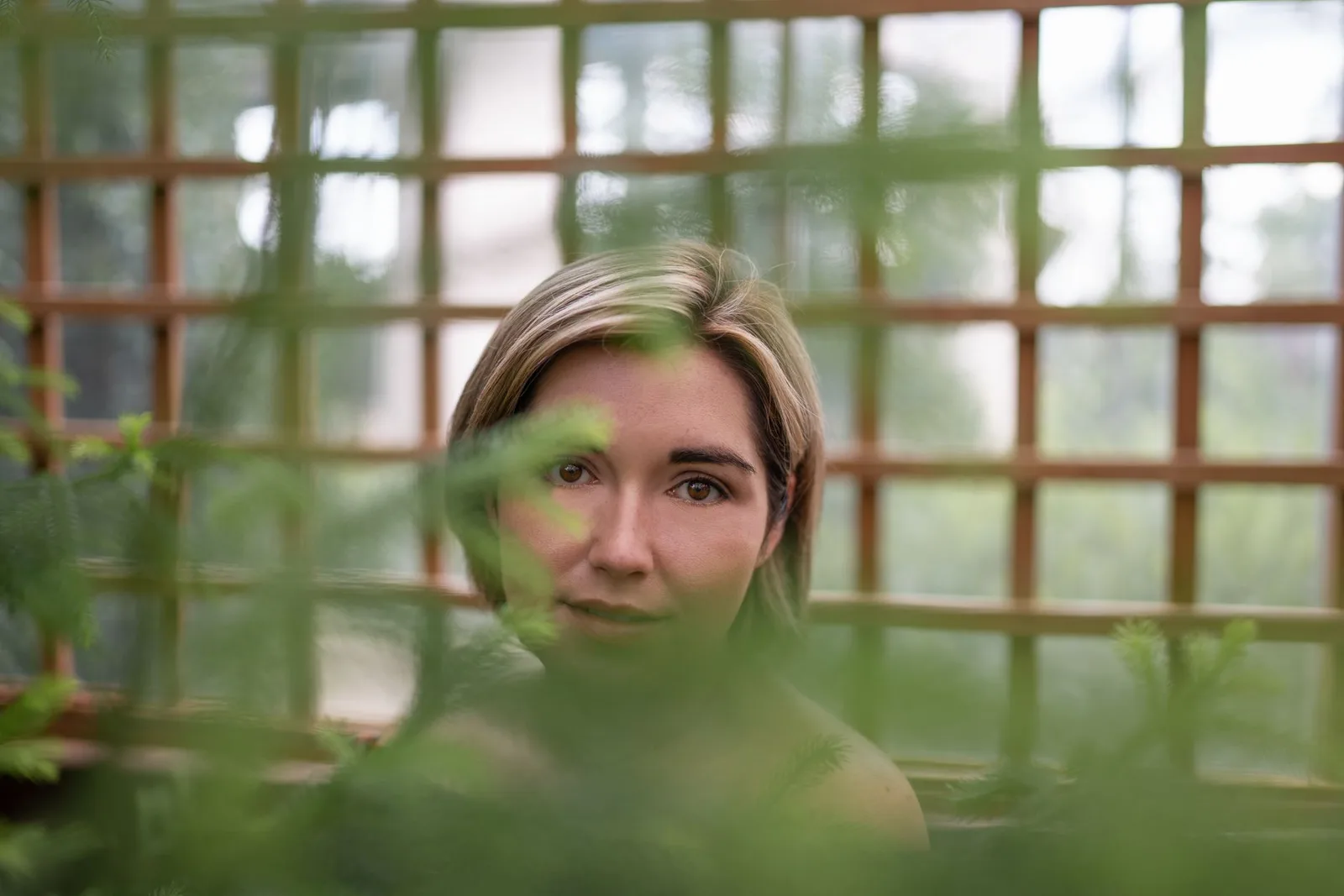 Portrait of a woman through lush foliage with natural soft light and green tones.