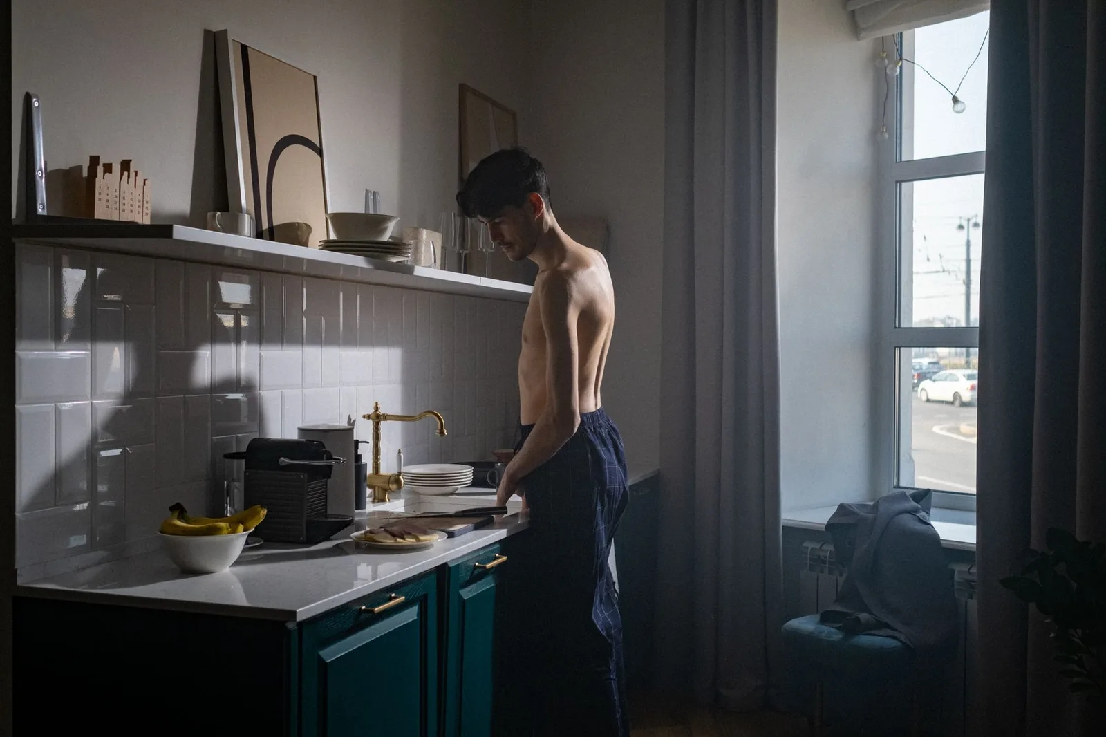 A shirtless man prepares breakfast in a sunlit kitchen during an early morning routine.