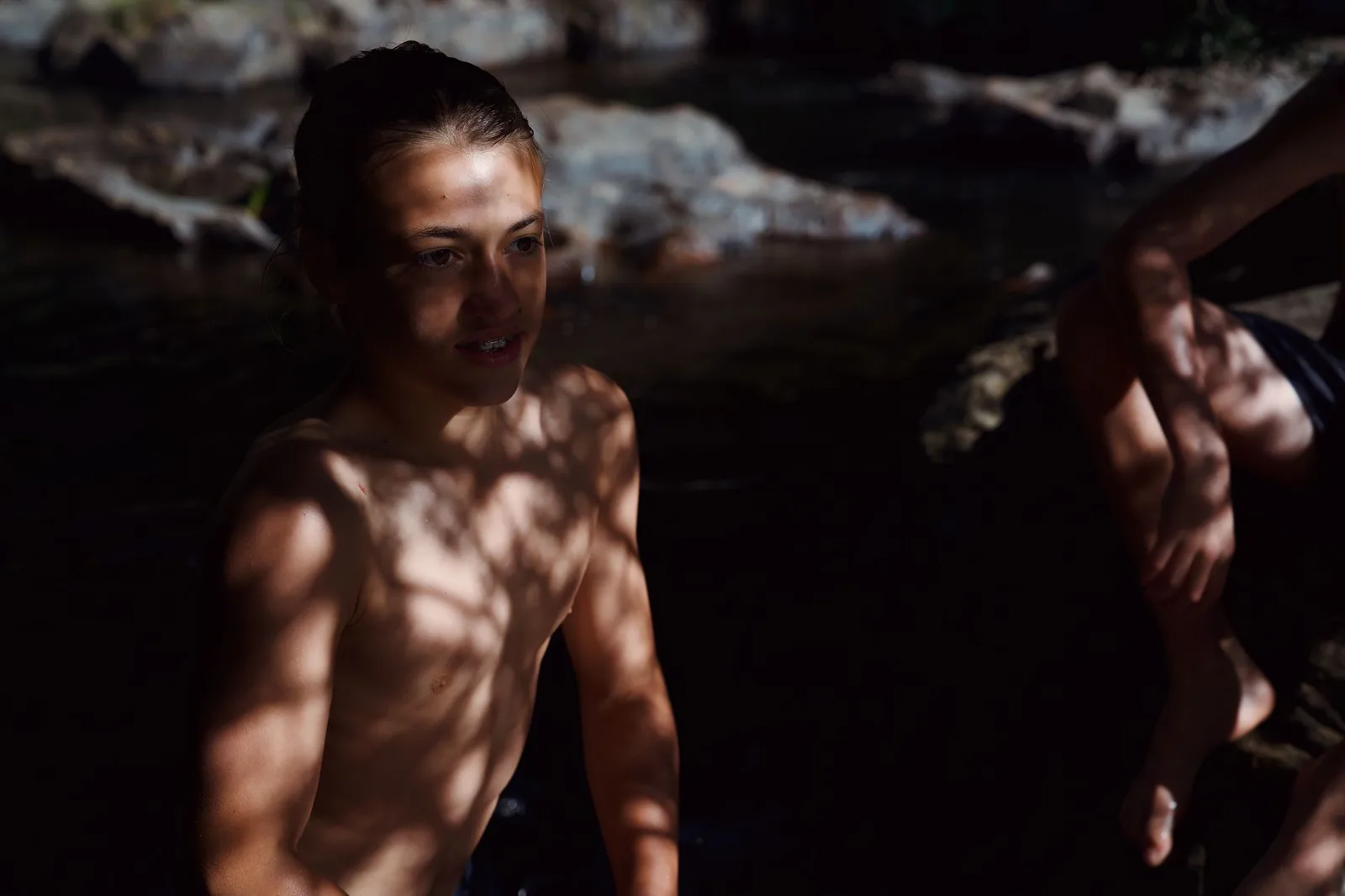 Teenager swimming in a shadowy natural water setting, highlighting tranquility.